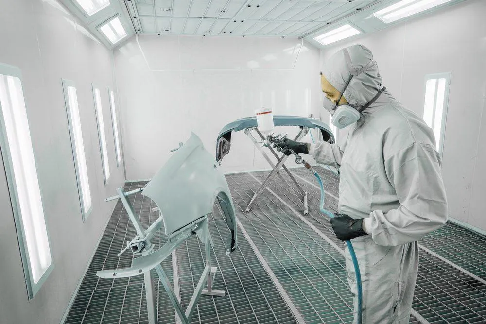 Automotive worker paints a car part in a paint booth. Photo: Shutterstock