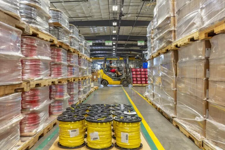 A KrisTech Wire employee drives a forklift past two rows of insulated copper wire products. A pallet of copper wire sits in the foreground.