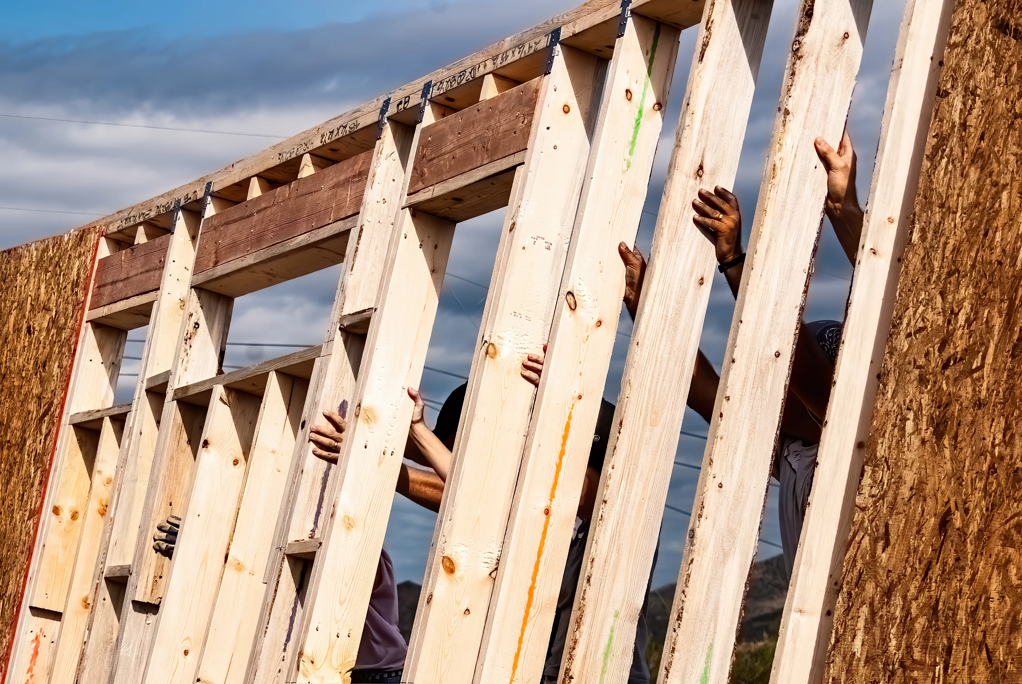 A group of volunteers stands up a wooden wall frame while building a home. Photo by Paul Christopherson.